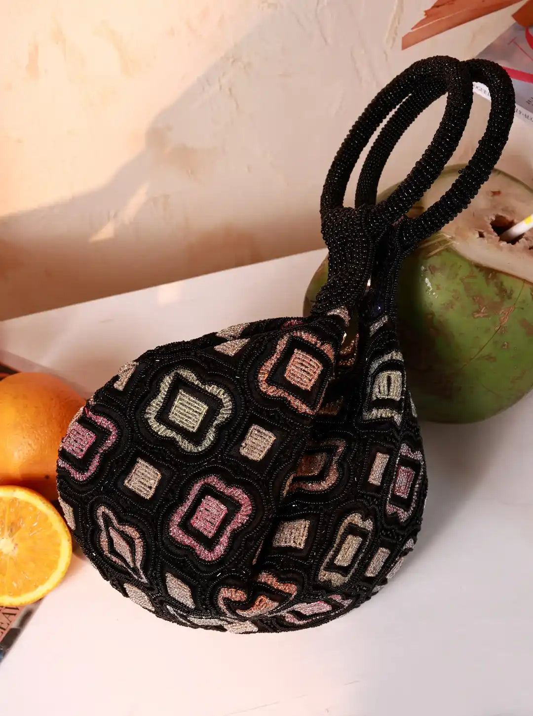 Black embroidered bag with geometric patterns on a light surface with fruits.