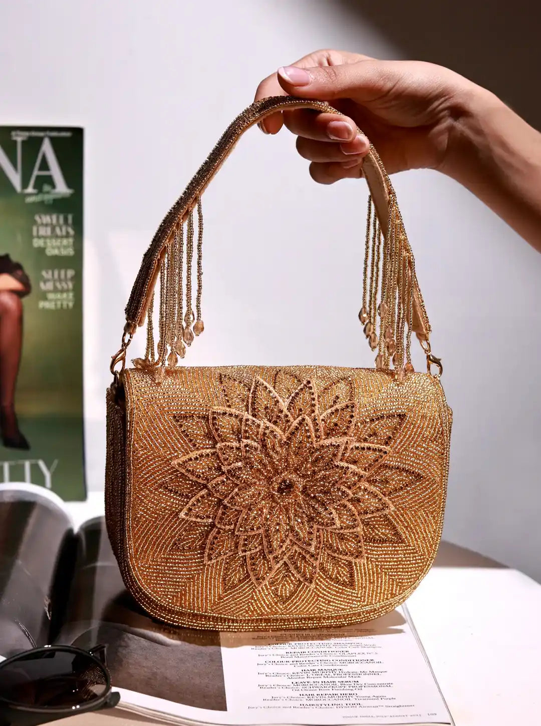 Gold beaded handbag held by a hand with a magazine and sunglasses in the background