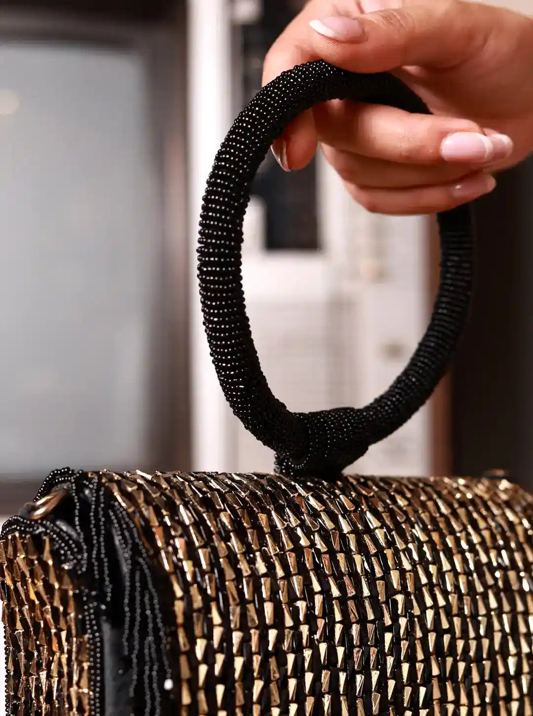 Hand holding a black beaded handle of a gold mesh handbag.