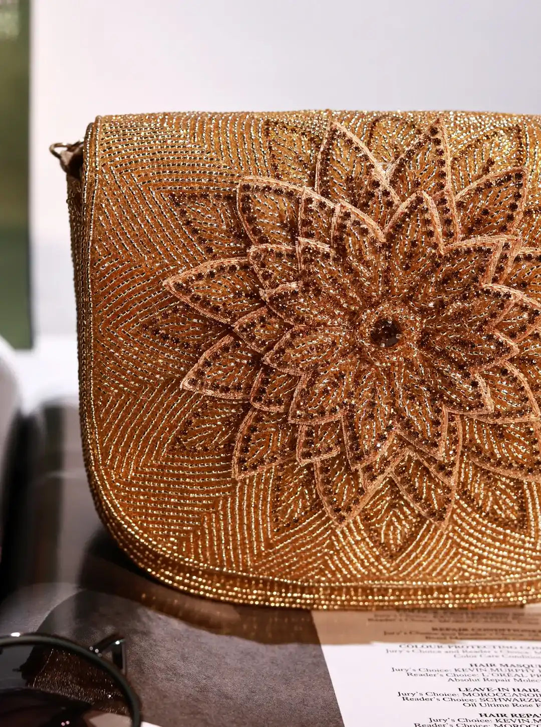 Gold beaded handbag with floral design on a reflective surface