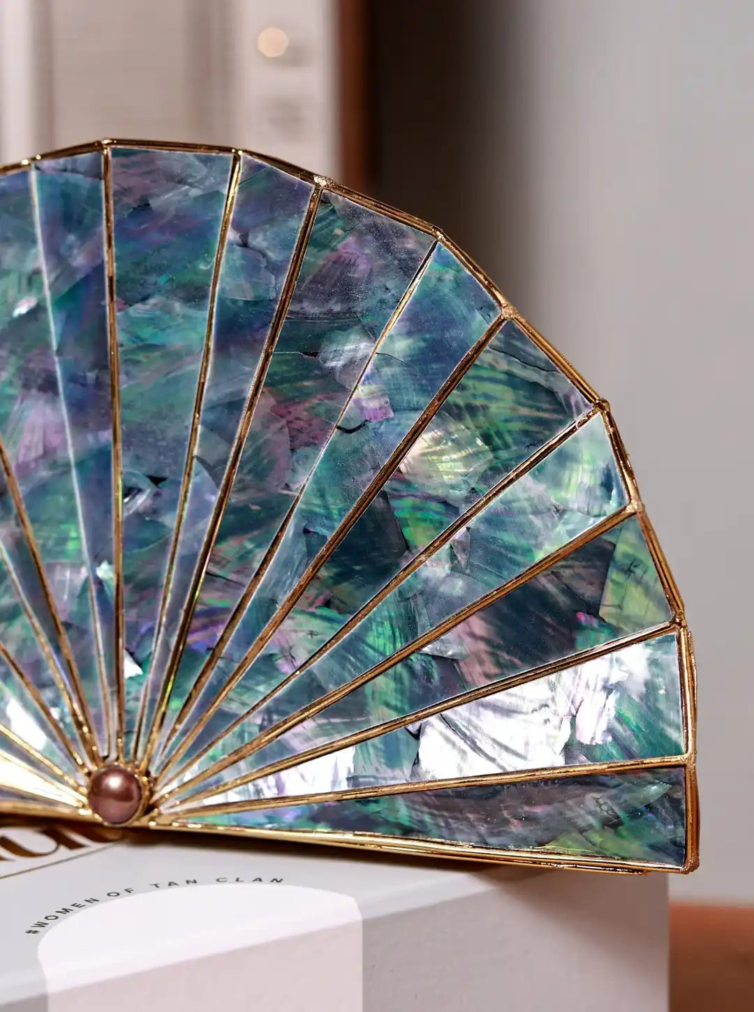 Decorative fan with iridescent blue and green panels on a white stand.