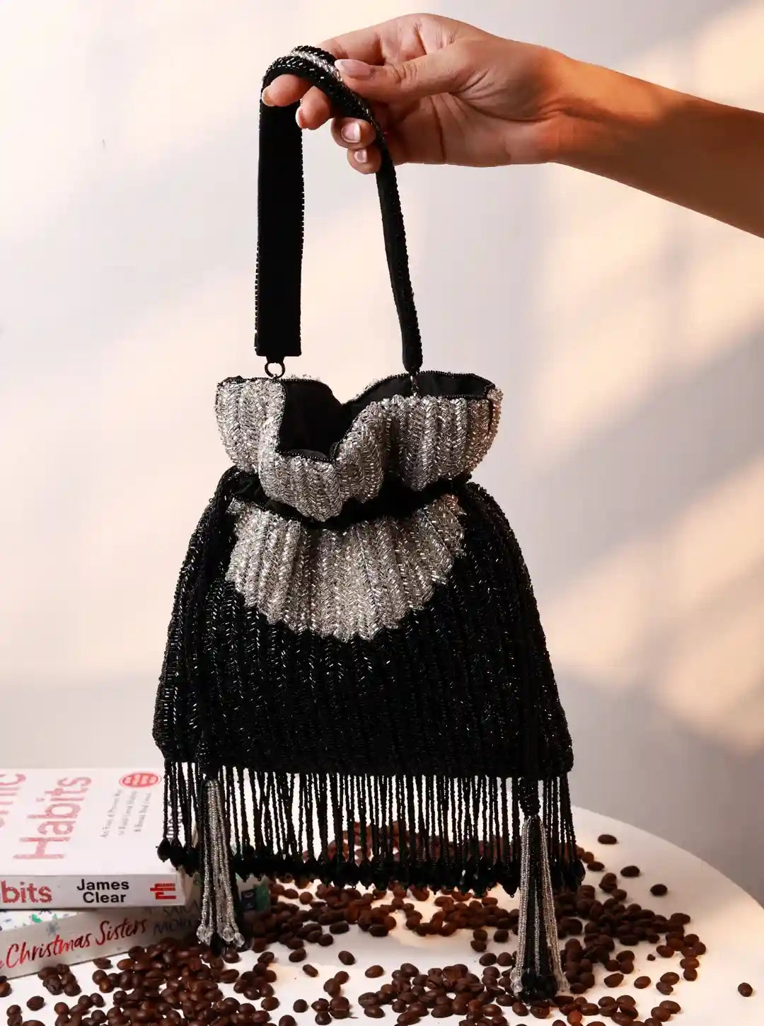 Black beaded handbag with fringe held above a surface with coffee beans and books.