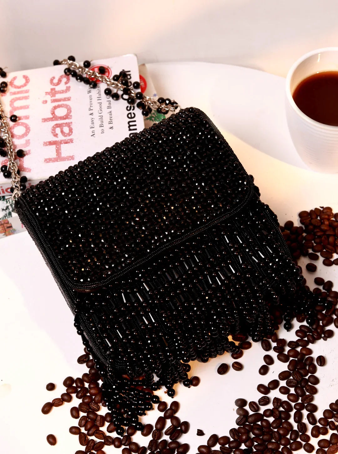 Black beaded clutch on a surface with coffee beans and a book titled 'Habits'.