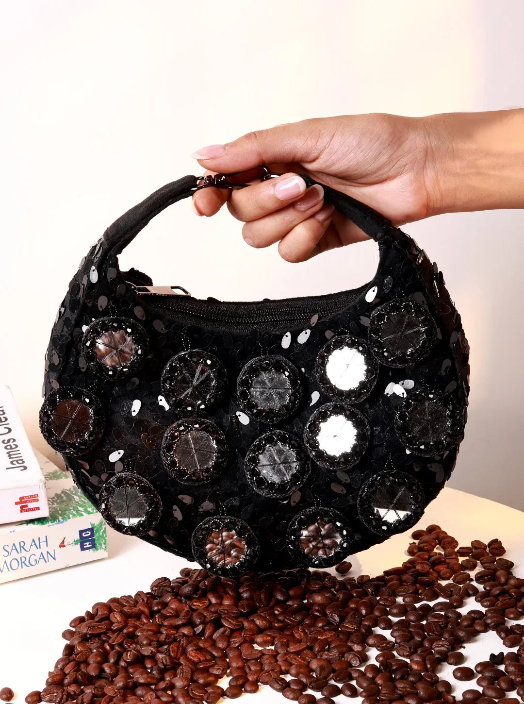 Black handbag with decorative stones held by a hand over coffee beans