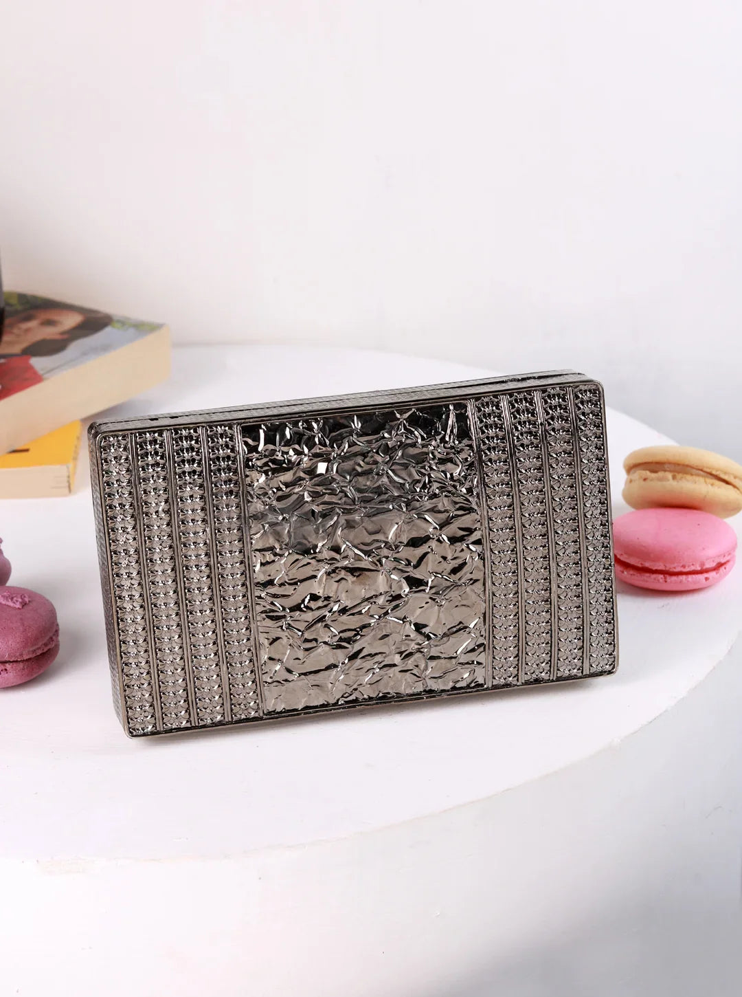 Silver clutch bag on a white surface with macarons in the background