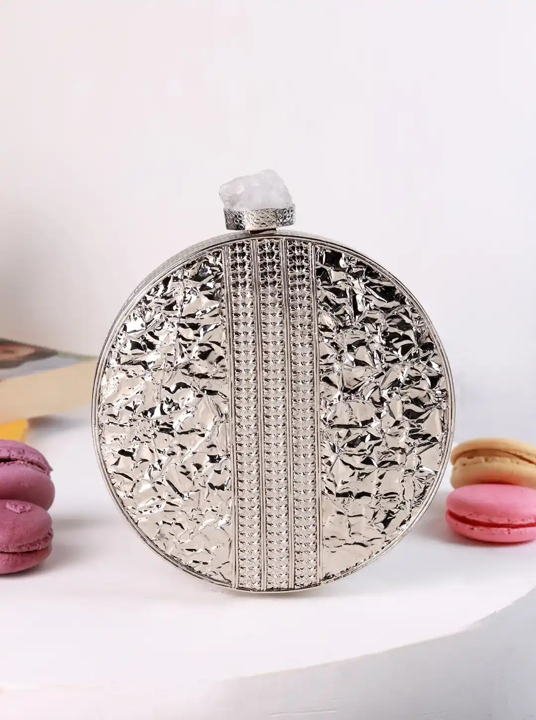Decorative round silver flask on a white surface with pink and yellow macarons.