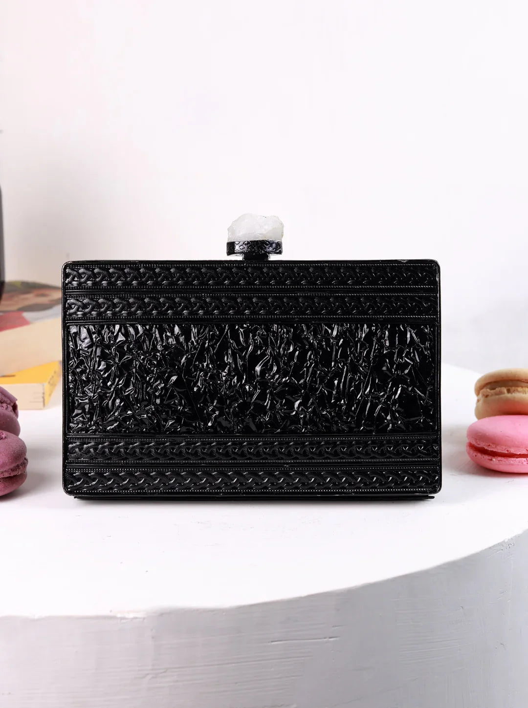 Black textured clutch bag on a white surface with macarons in the background