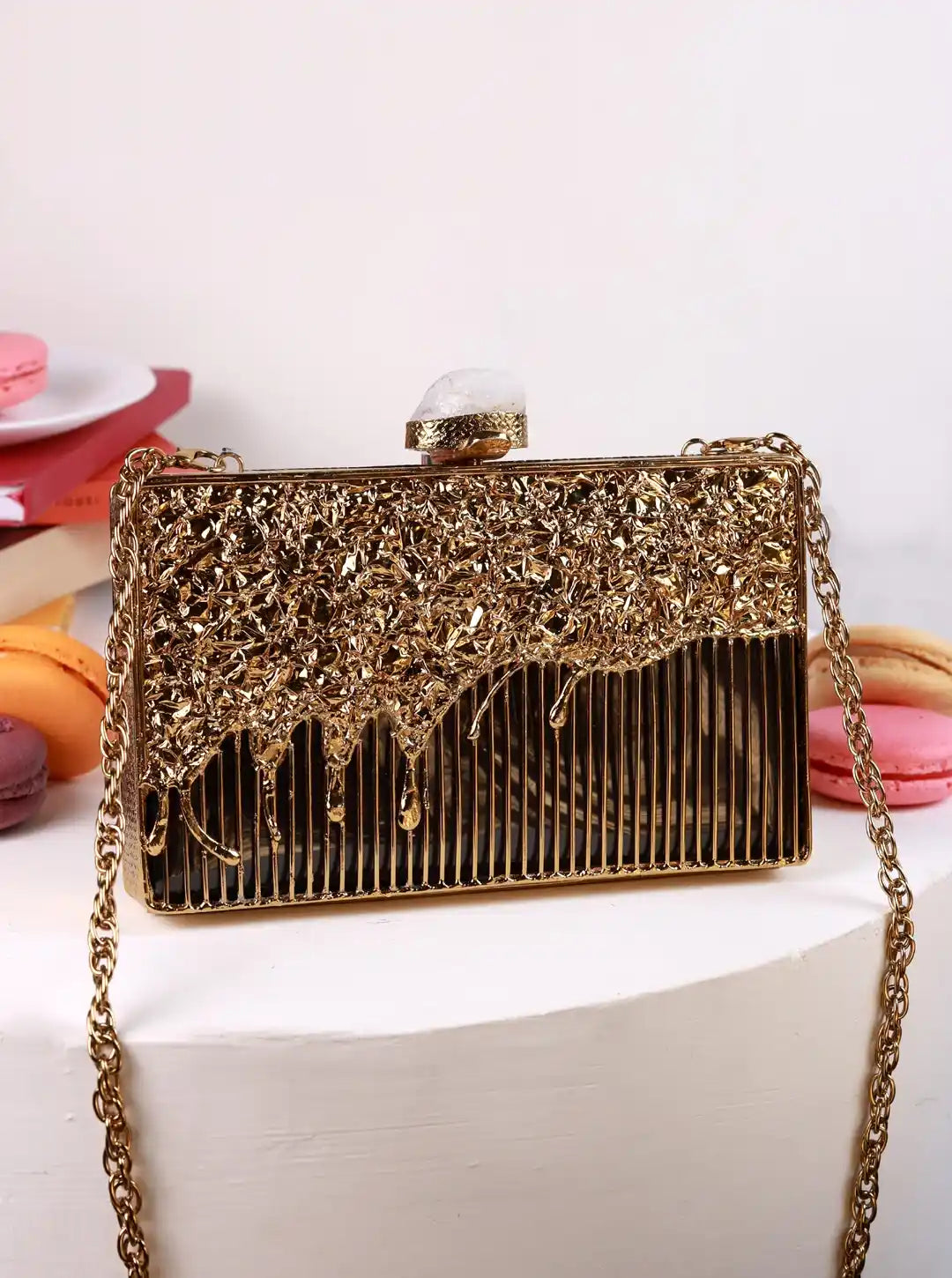 Gold clutch bag with intricate design on a white surface with colorful macarons in the background