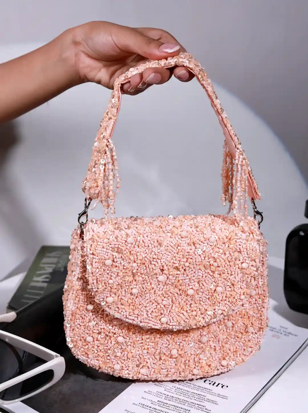 Hand holding a pink beaded handbag on a light gray background