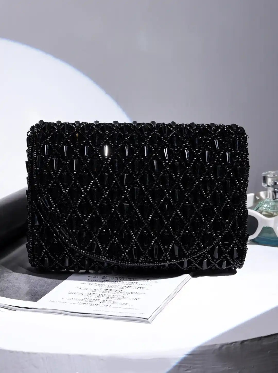 Black woven clutch bag on a gray surface with a white background