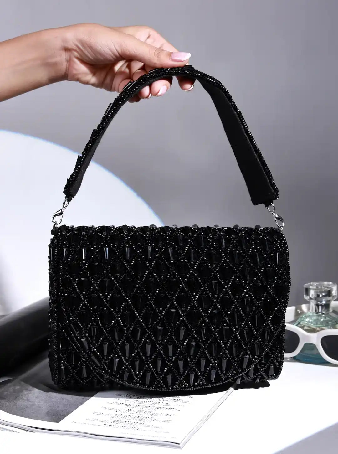 Black textured handbag held by a hand on a gray background