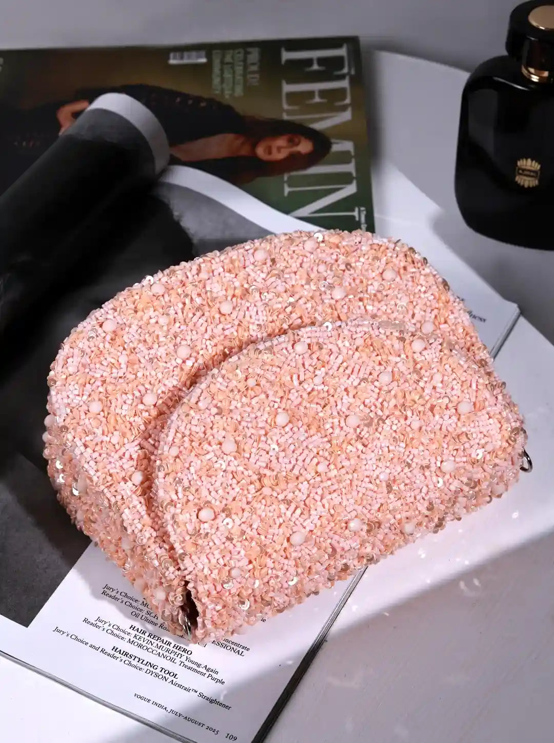 Pink glittery clutch bag on a magazine with a bottle of perfume in the background
