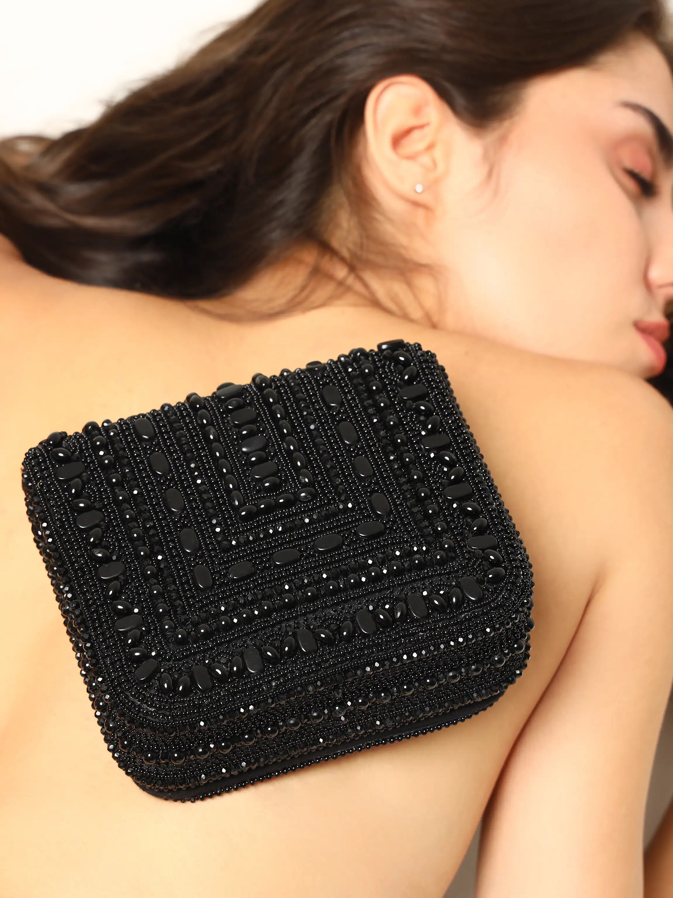 Black beaded clutch held by a woman against a neutral background