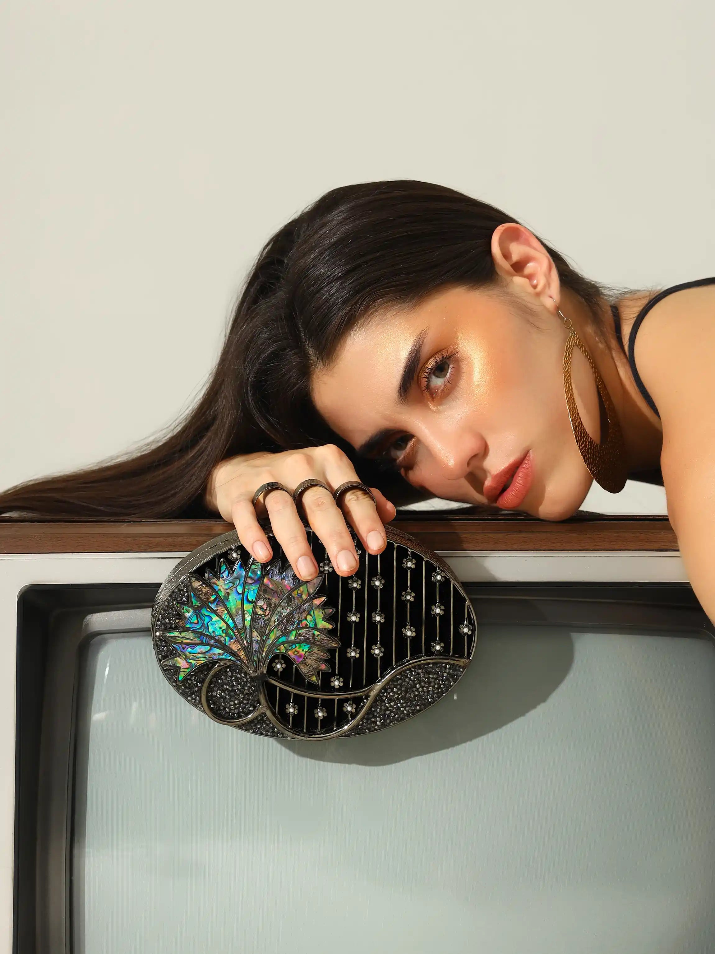 Woman holding a decorative clutch in front of an old television set