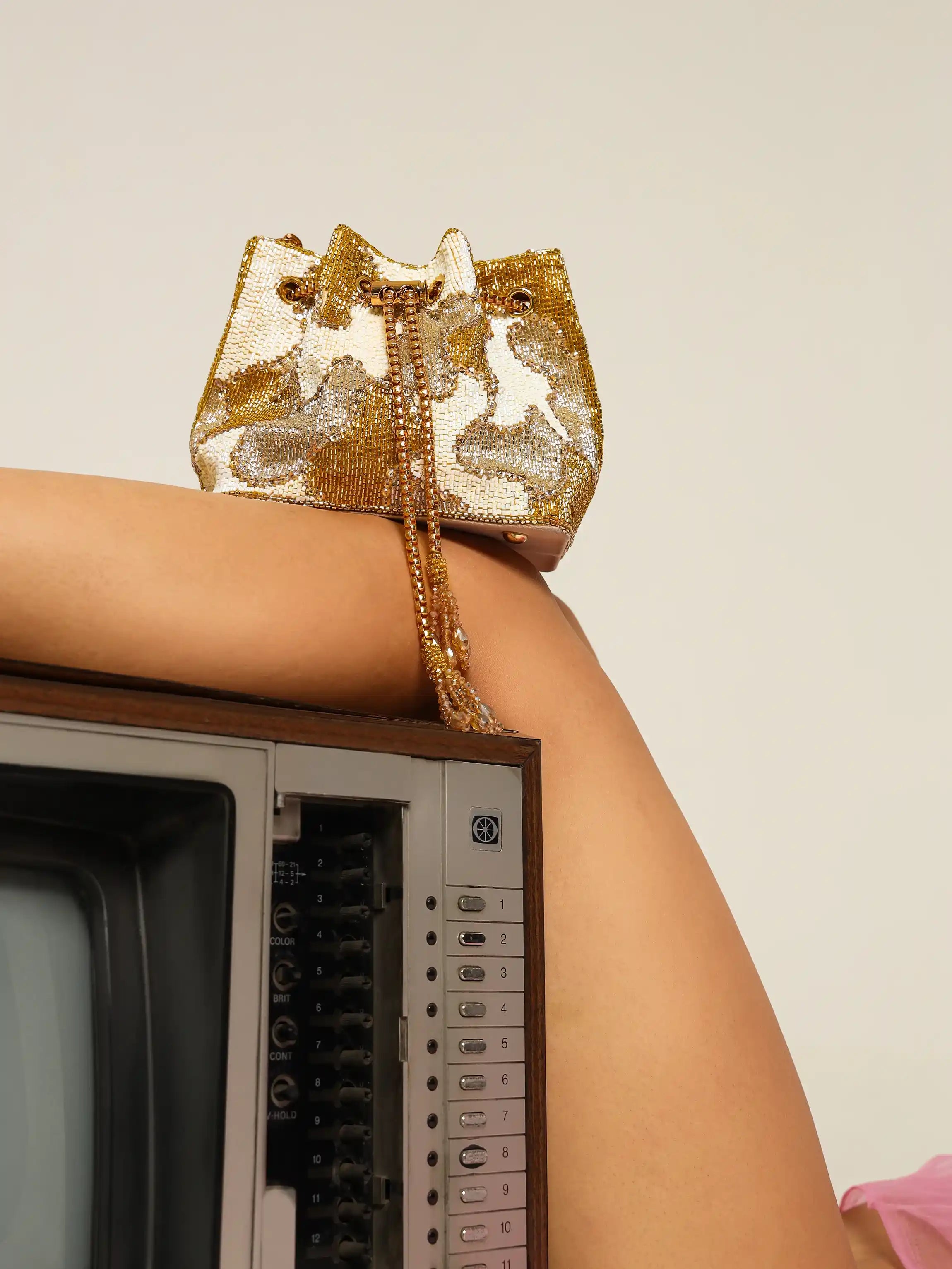Gold sequin handbag held by a person with a vintage television set in the background
