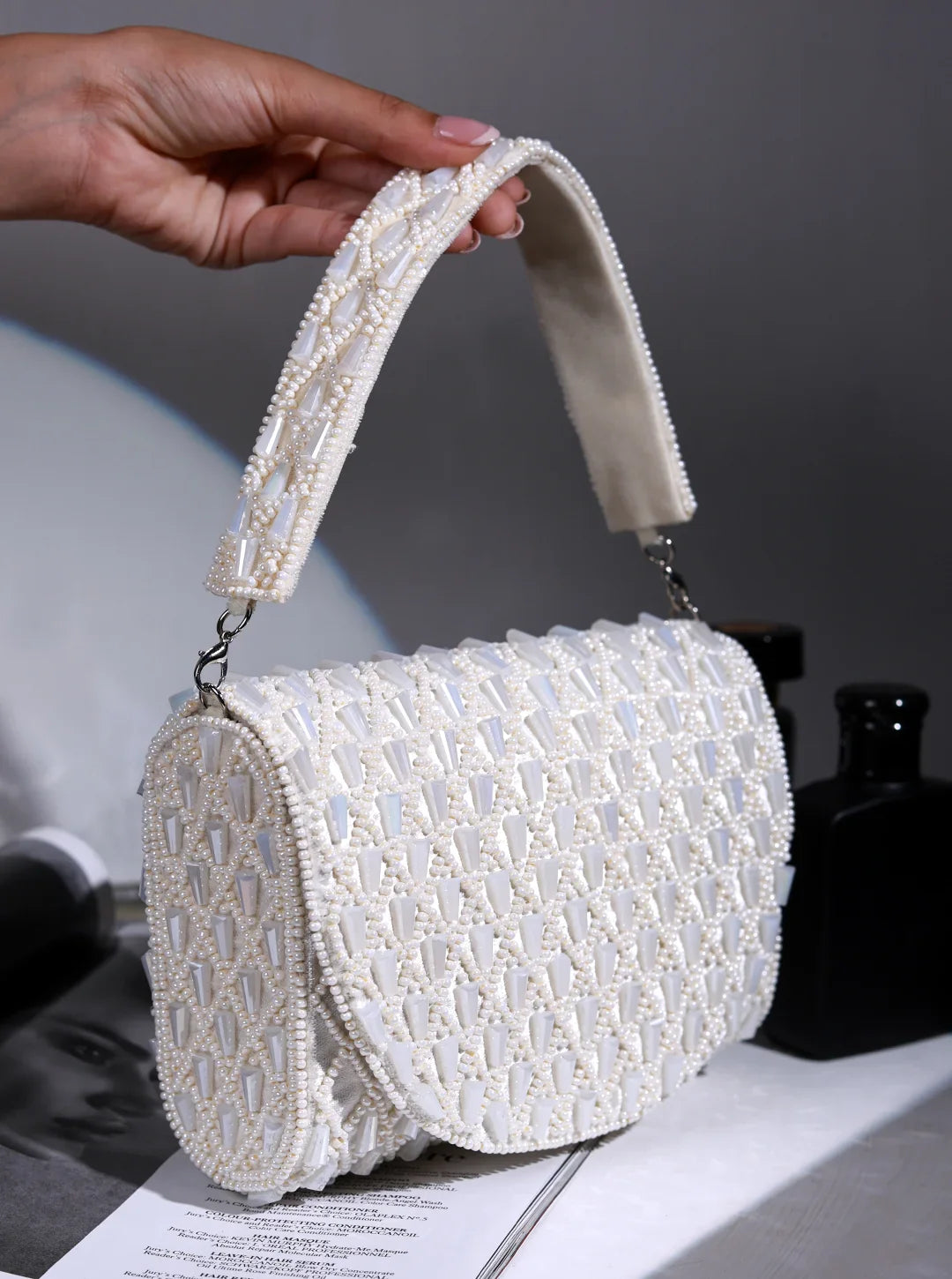 White beaded handbag held by a hand on a gray background
