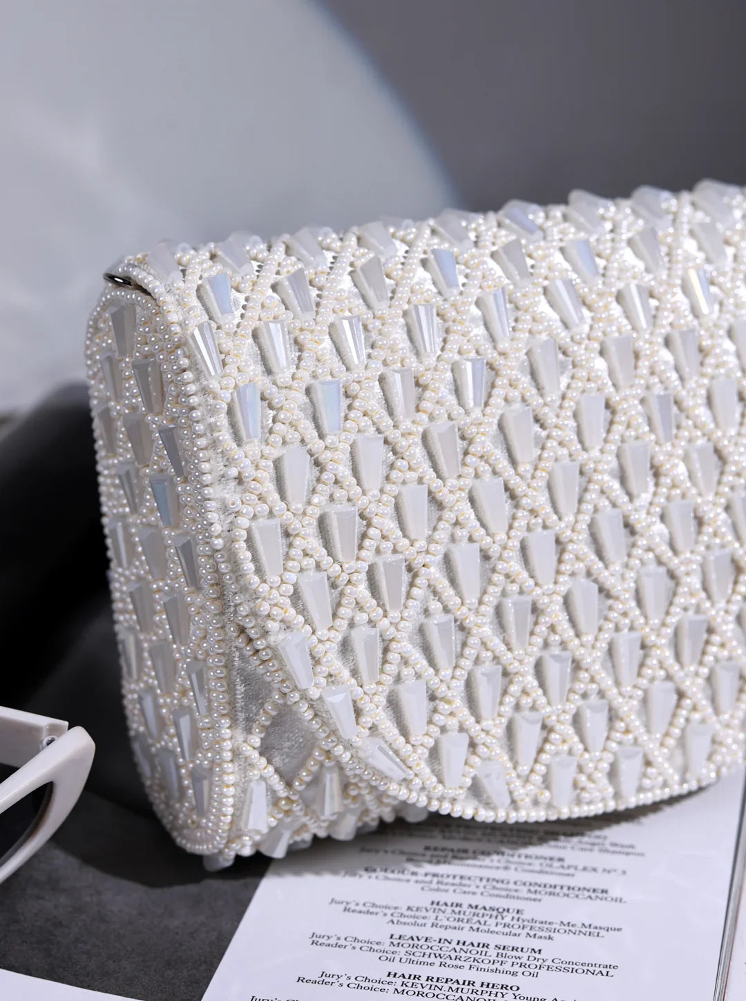 White beaded clutch bag on a gray surface with a blurred background