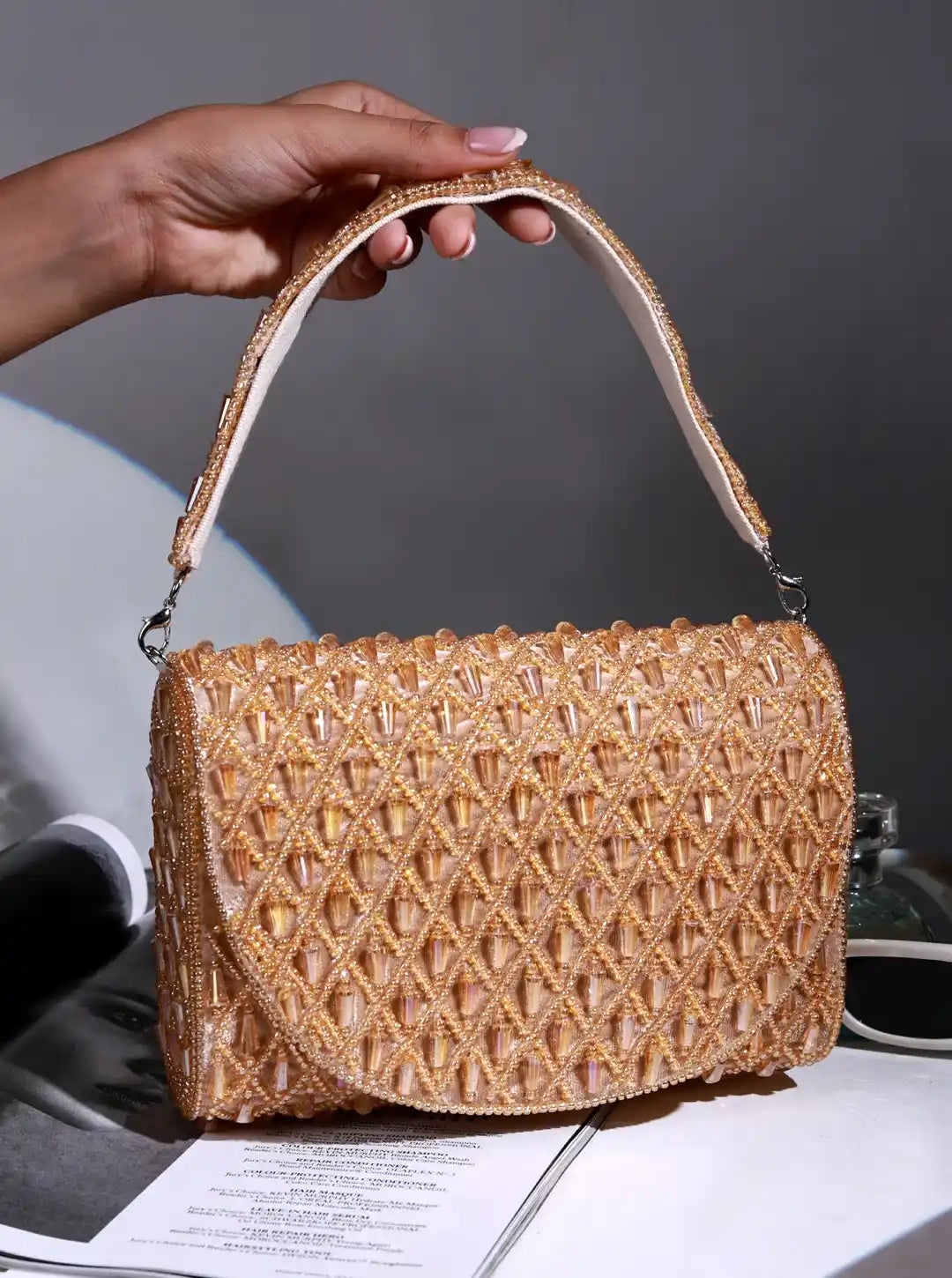 Hand holding a woven handbag on a magazine with a gray background