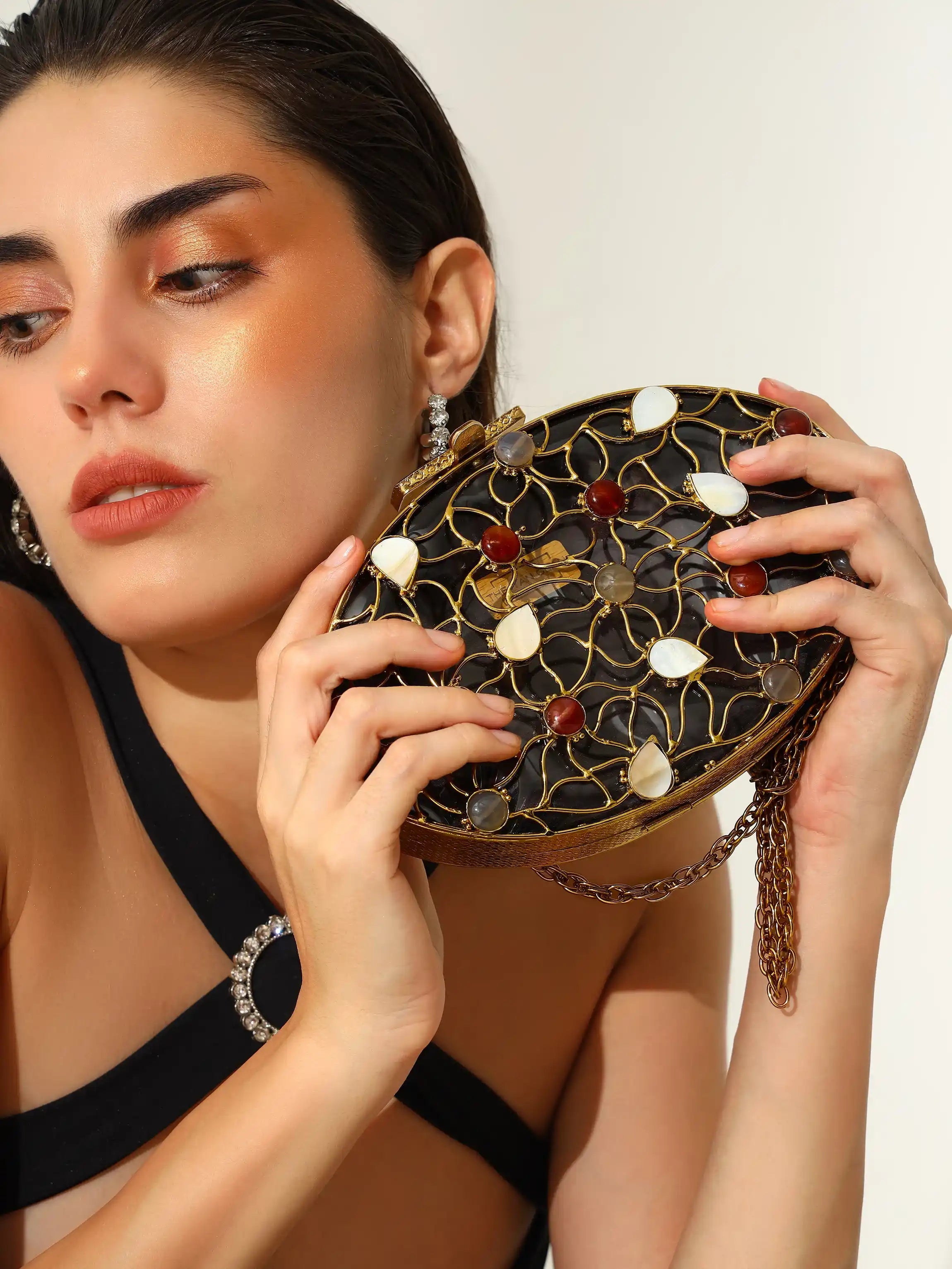 Woman holding a decorative handbag with intricate design and gemstones.
