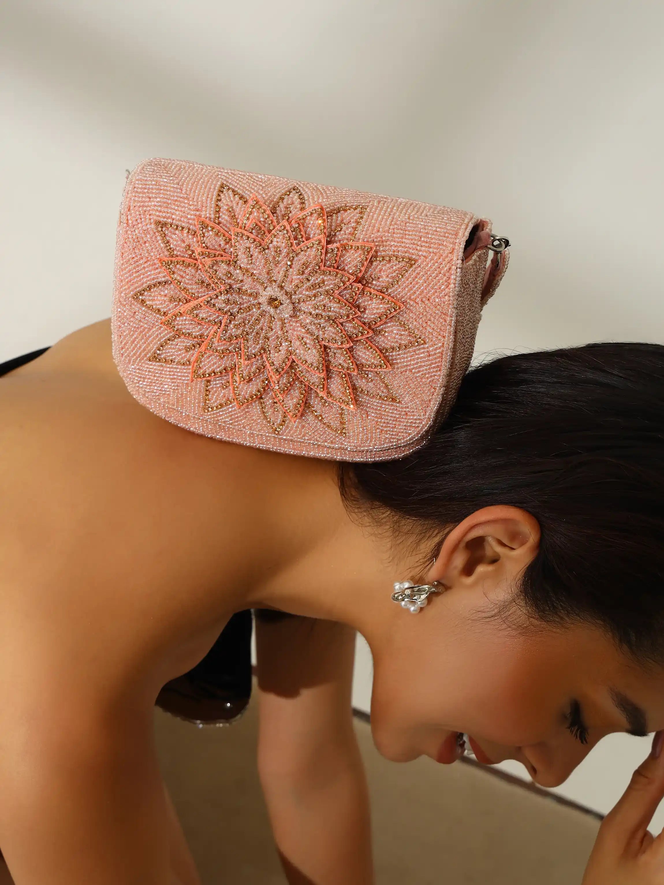Woman wearing a pink beaded handbag with a floral design on her shoulder against a neutral background