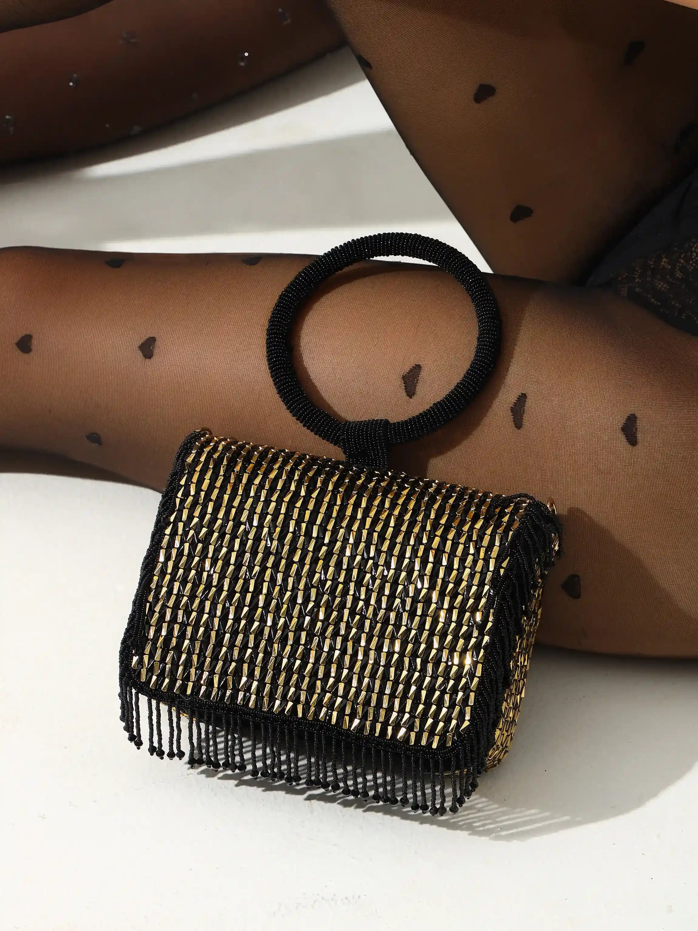 Black beaded clutch bag on a white surface with a person wearing black heart-patterned tights.