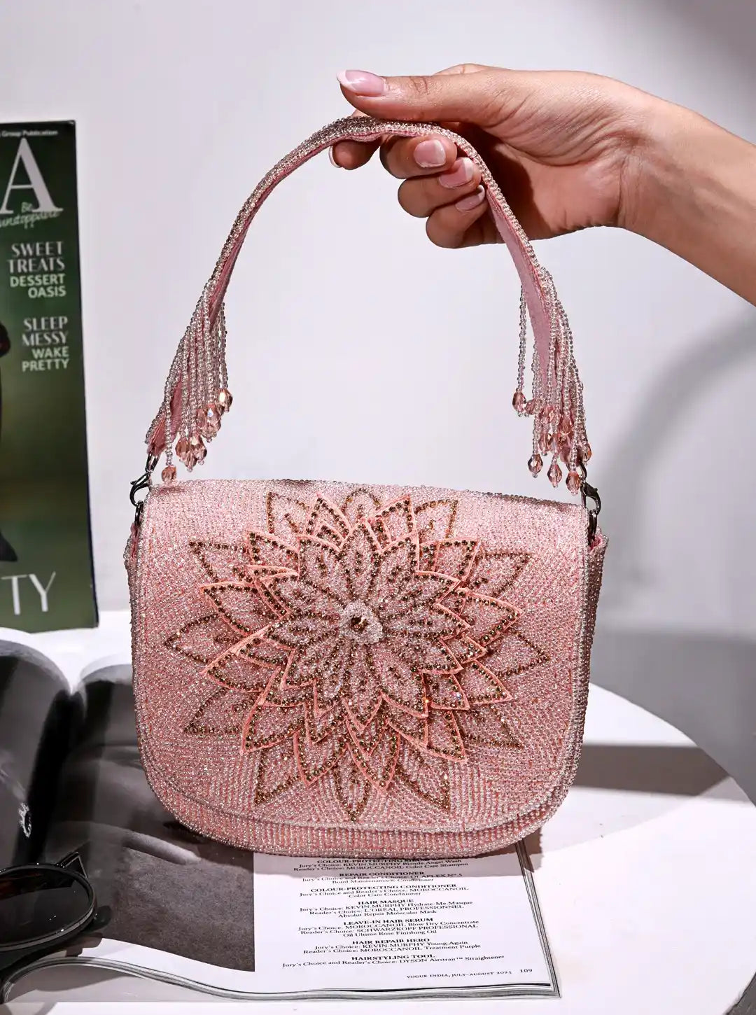 Pink beaded handbag held by a hand on a white surface with a magazine underneath.