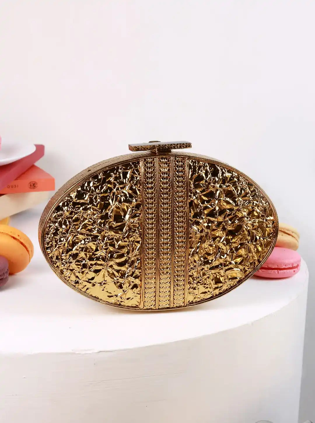 Gold clutch bag on a white surface with colorful macarons in the background