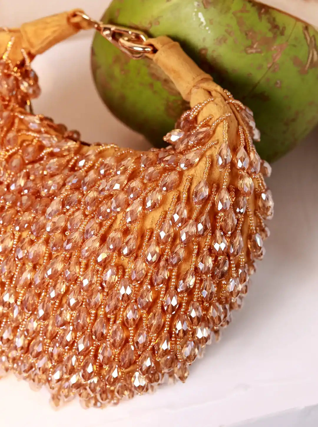 Close-up of a gold beaded handbag with a green fruit in the background