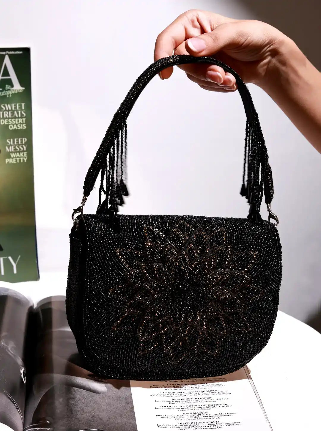 Black beaded handbag held by a hand on a magazine background