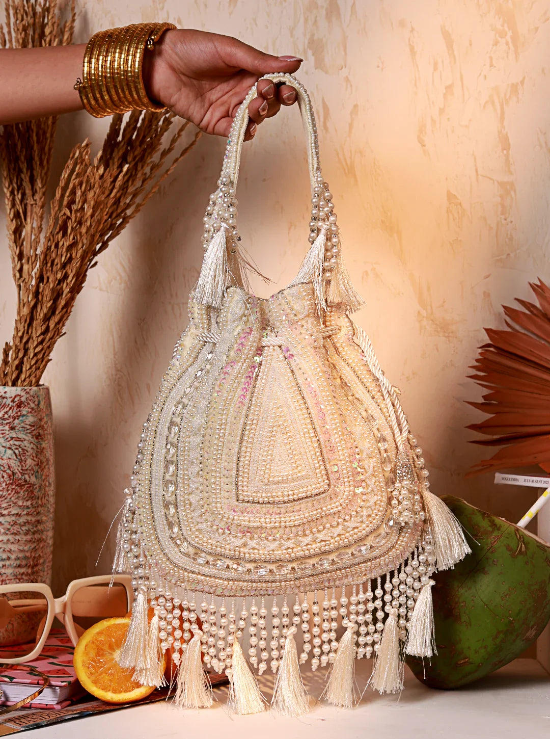 Handbag with intricate beading and tassels held by a hand against a warm-toned background.