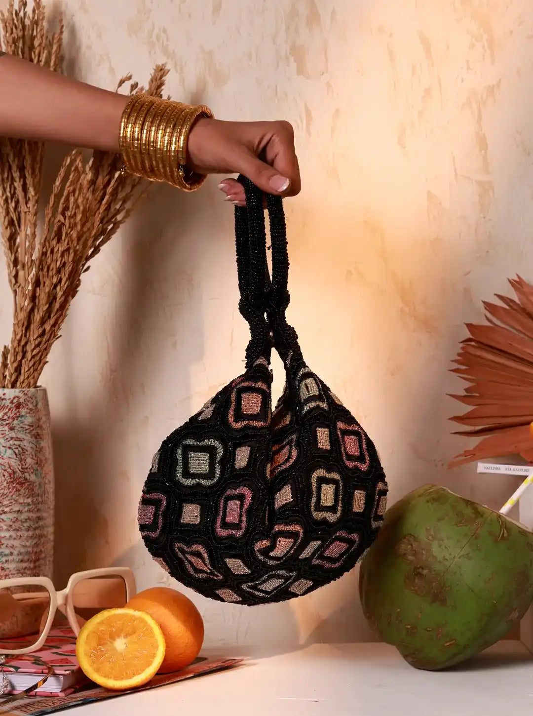 Hand holding a patterned black bag with oranges and a coconut on a table.