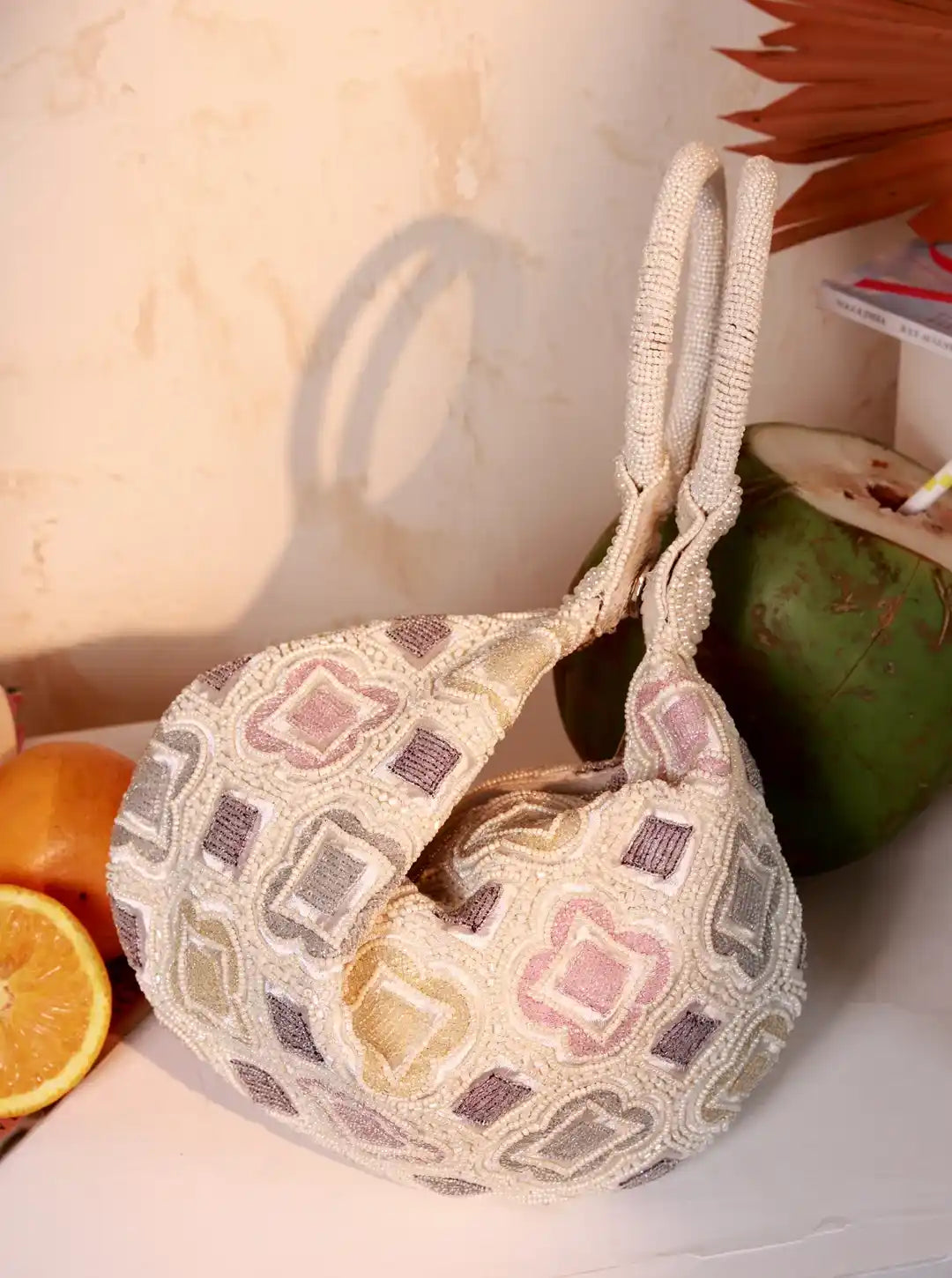 Woven bag with geometric pattern next to a coconut and oranges on a light surface.