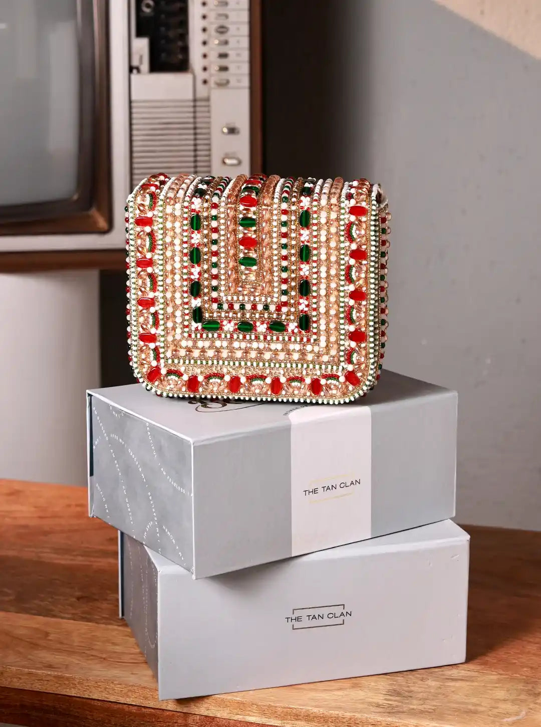 Decorative handbag with gemstones on a box labeled 'The Tan Clan' in a room setting.