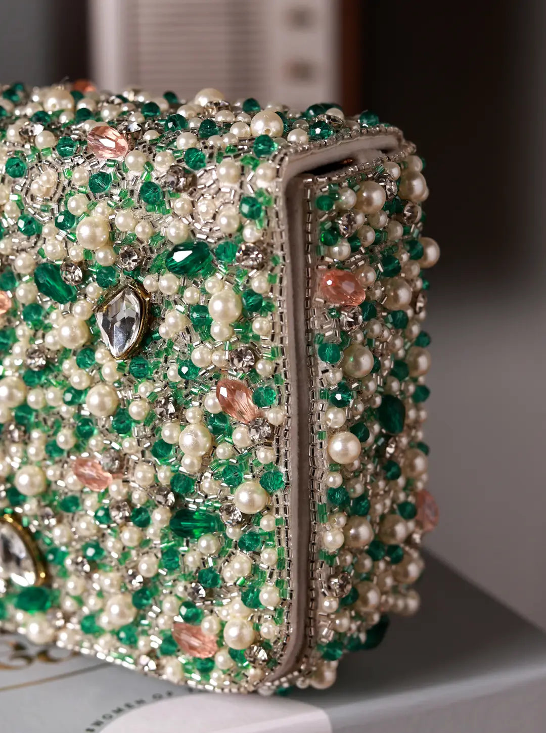 Close-up of a beaded clutch with green and white stones on a blurred background