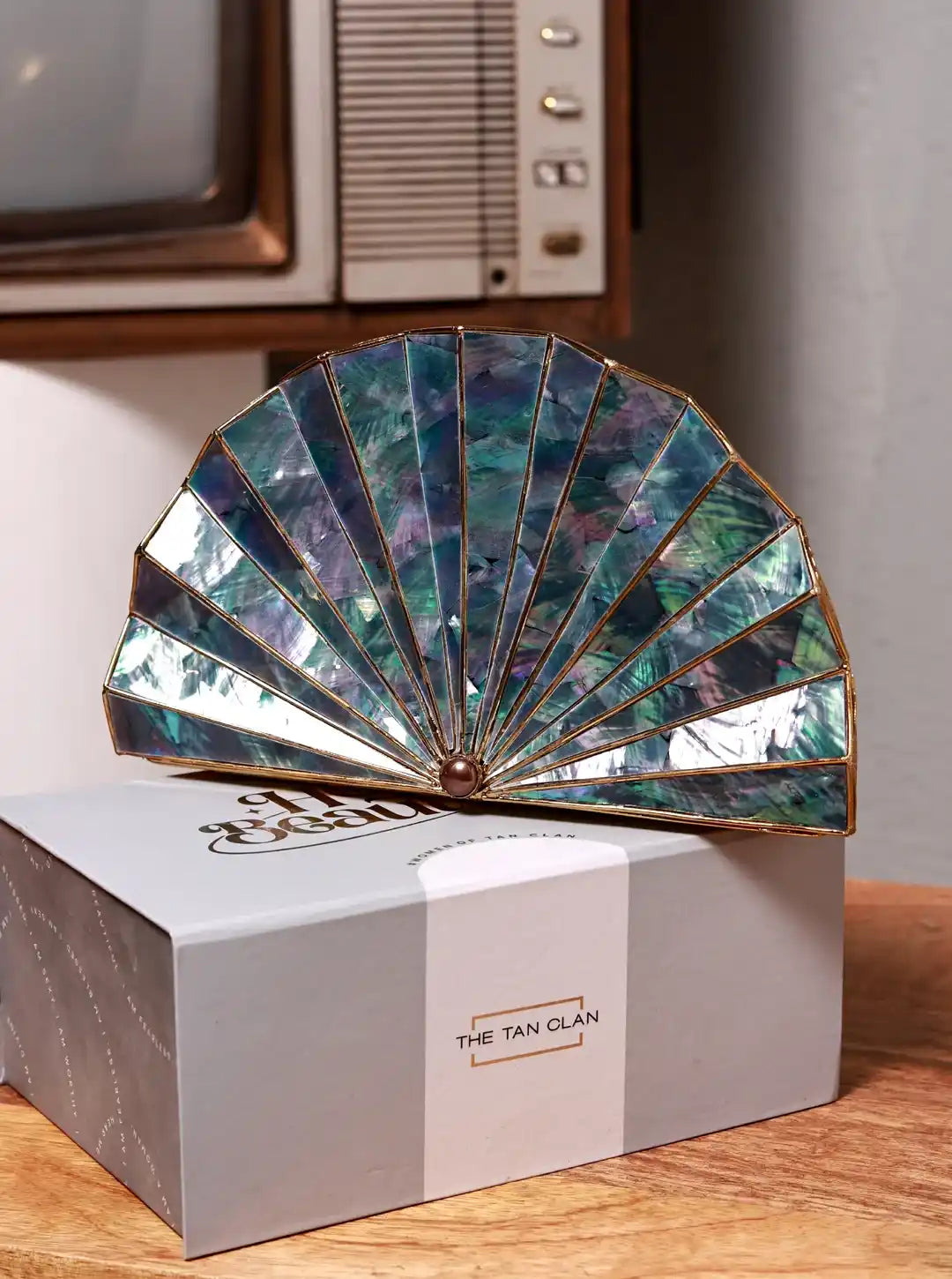 Decorative fan with iridescent colors on a box labeled 'The Tan Clan' in a vintage setting.