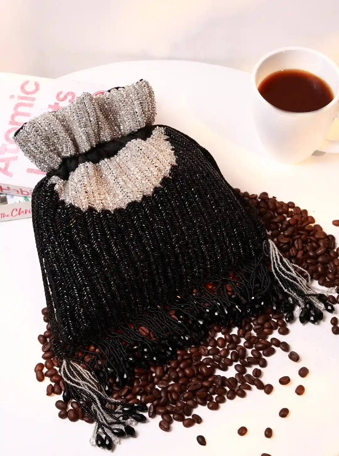 Black and gray beaded hot water bottle on a surface with coffee beans and a cup of coffee.