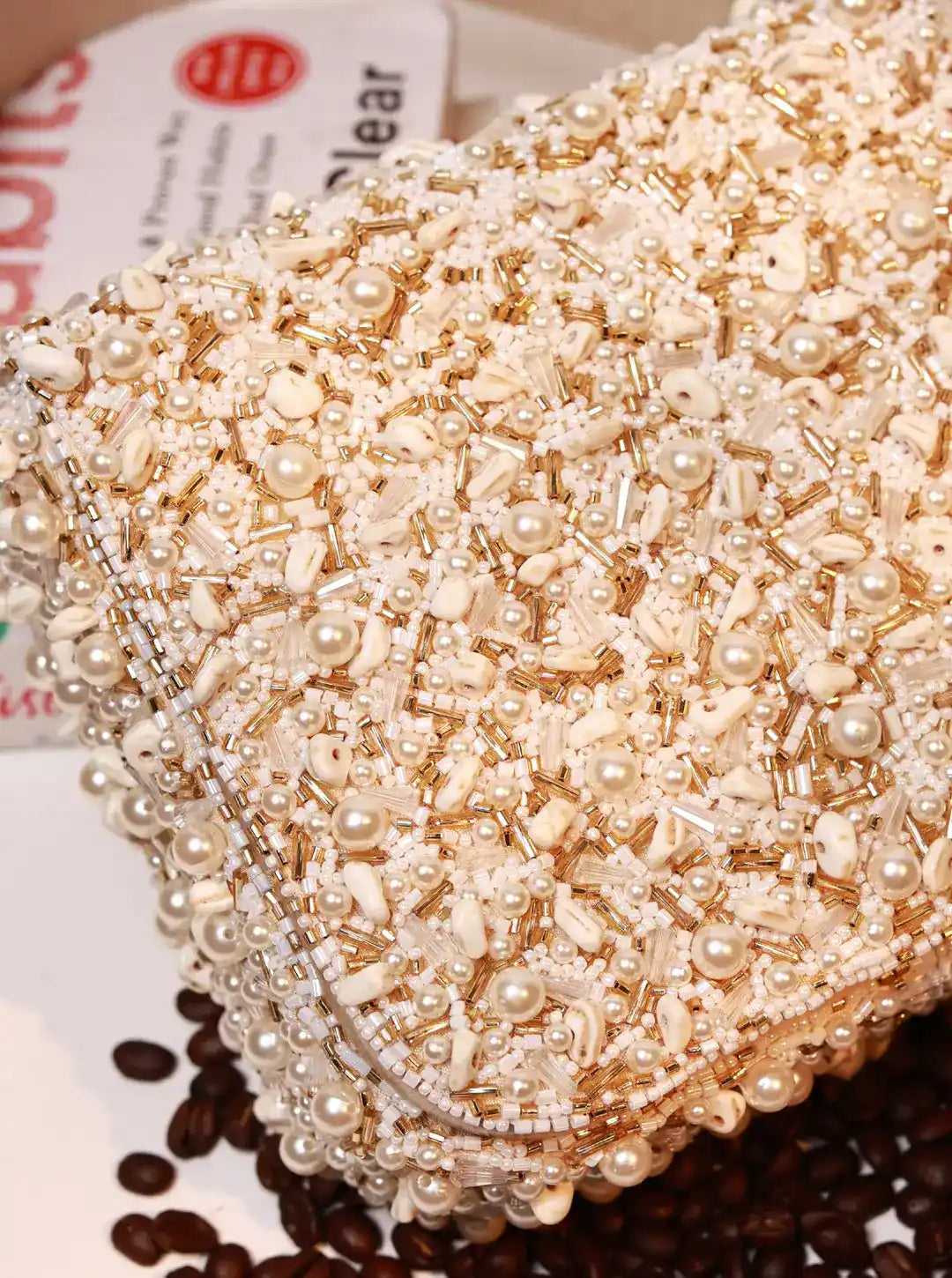 Close-up of a beaded clutch bag with pearls on a surface with coffee beans.