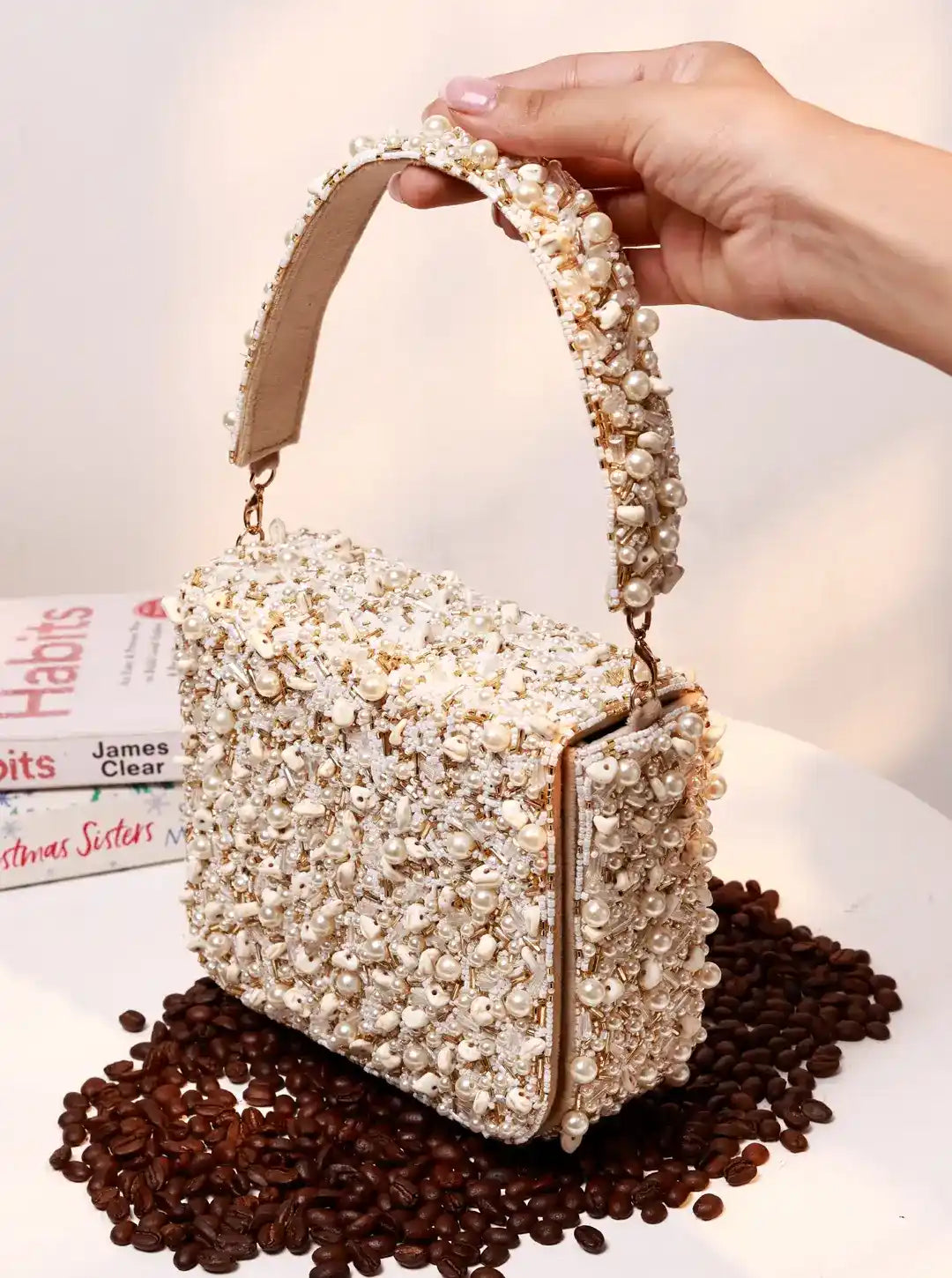 Handbag with pearl handle held by a hand on a surface with coffee beans