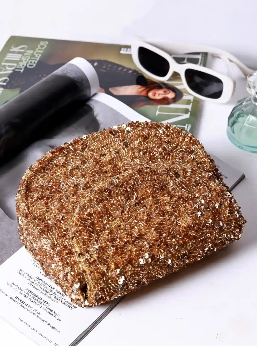 Gold sequin clutch on a magazine with sunglasses and a bottle cap.