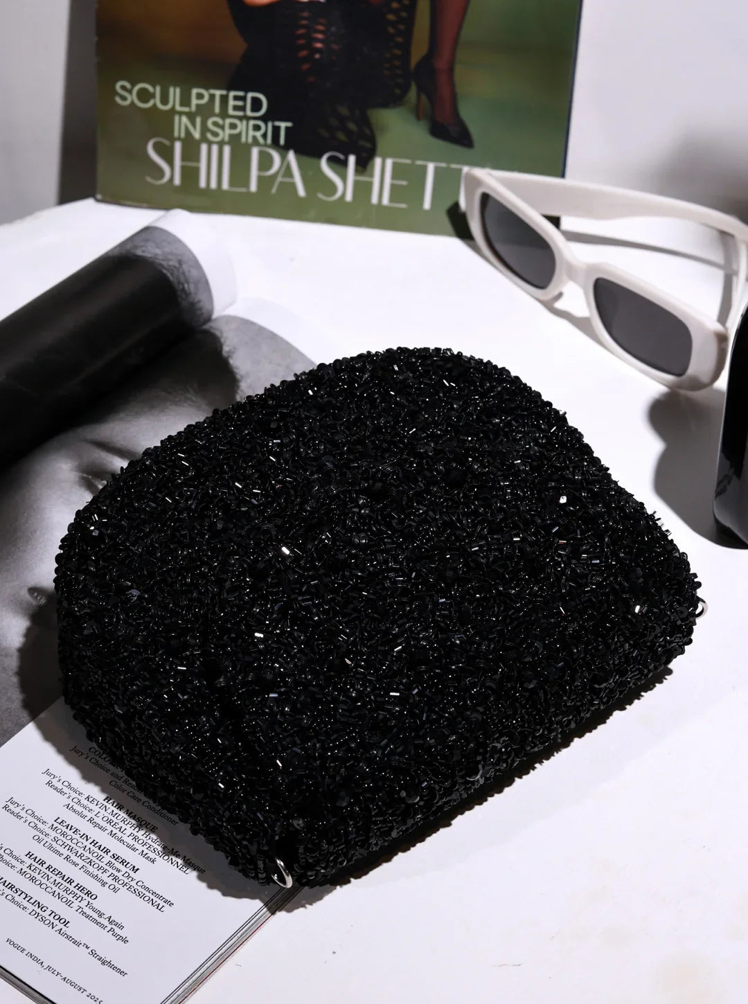 Black textured pouch on a magazine with sunglasses and a poster in the background