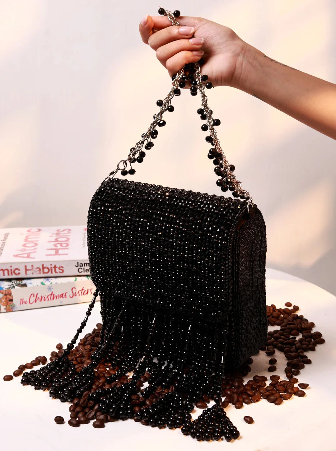 Black beaded handbag held by a hand with coffee beans on a white surface.