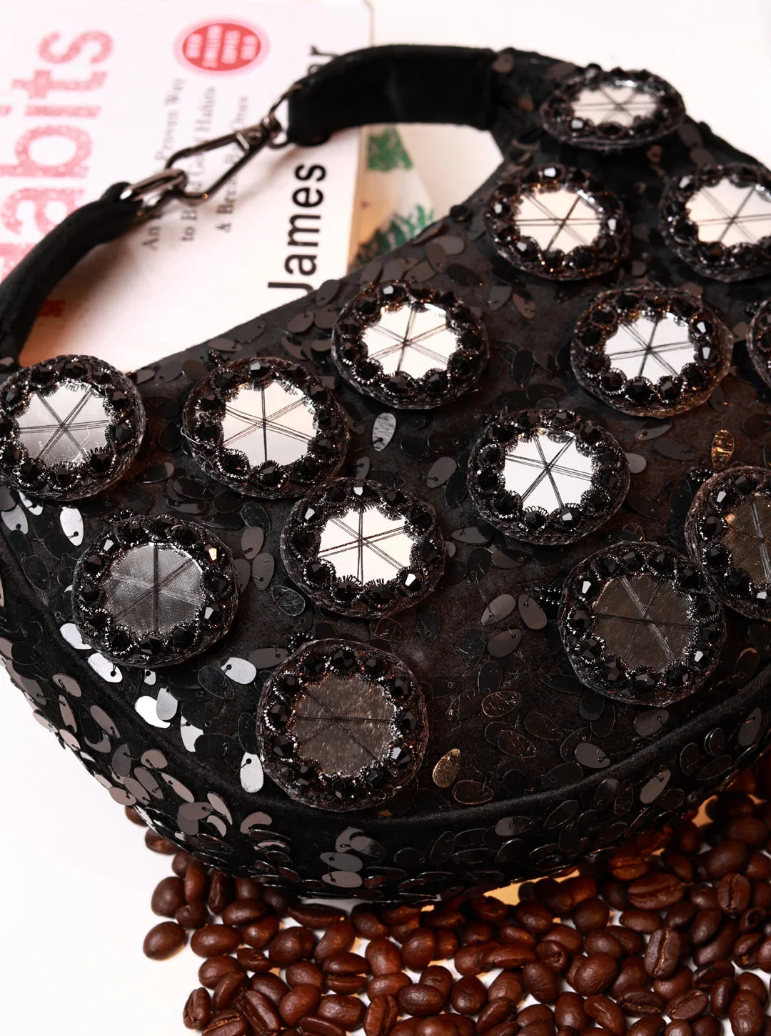 Black handbag with decorative studs on a surface with coffee beans