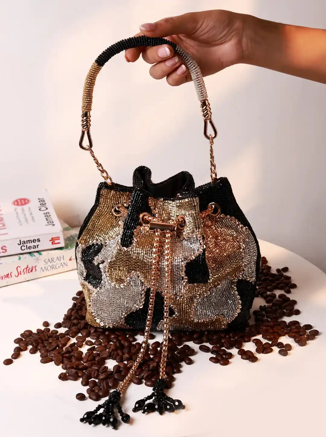 Handbag with decorative handle held by a hand on a surface with coffee beans