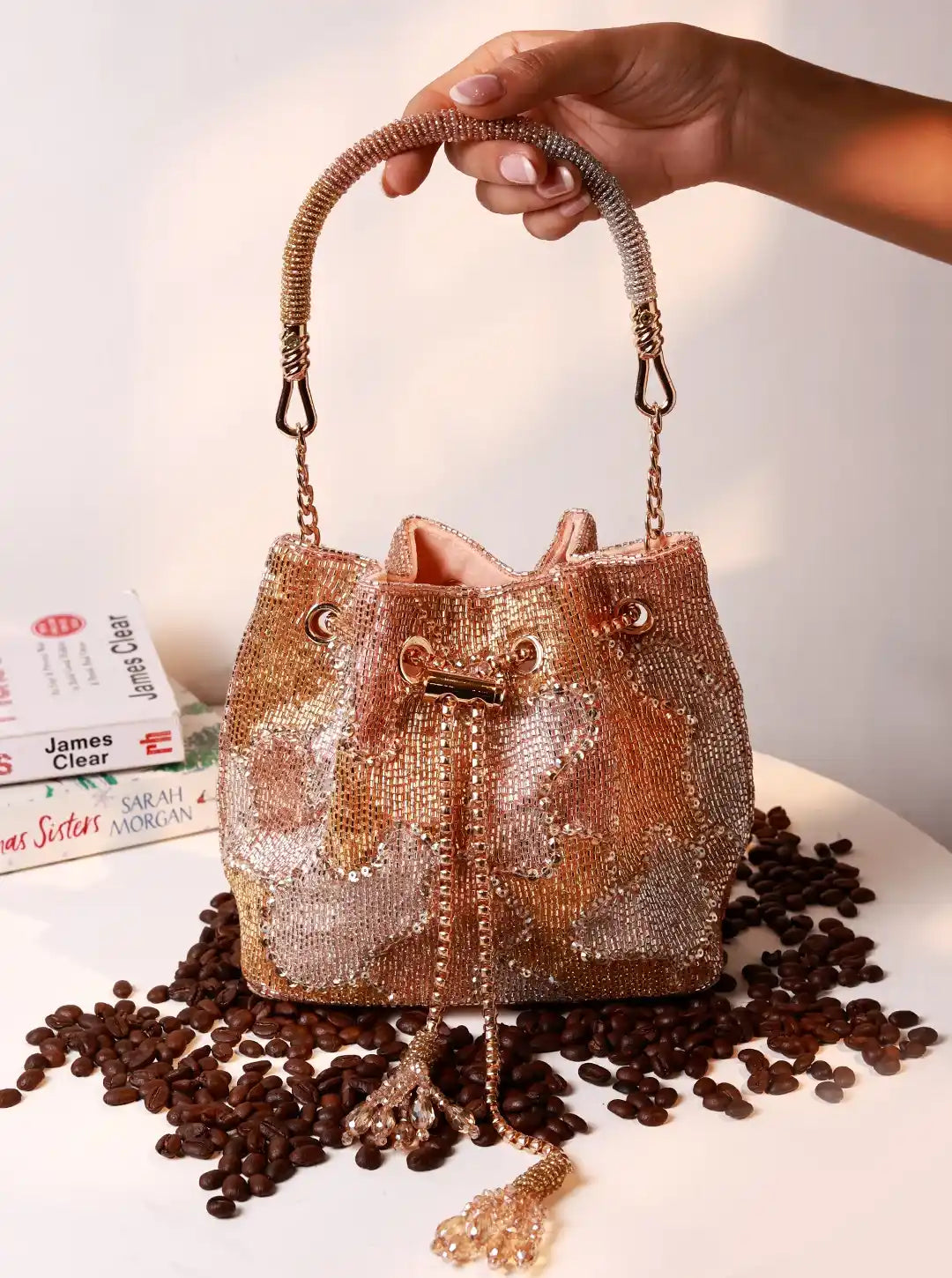 Handbag with rhinestone details held by a hand on a surface with coffee beans.