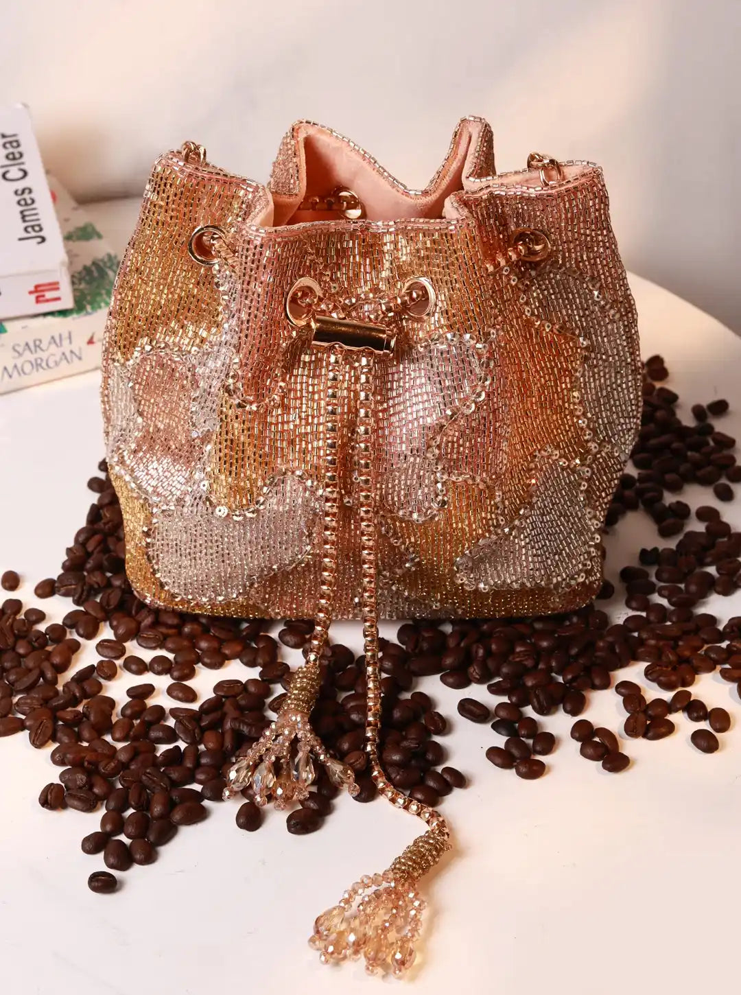 Rose gold beaded handbag on a white surface with coffee beans