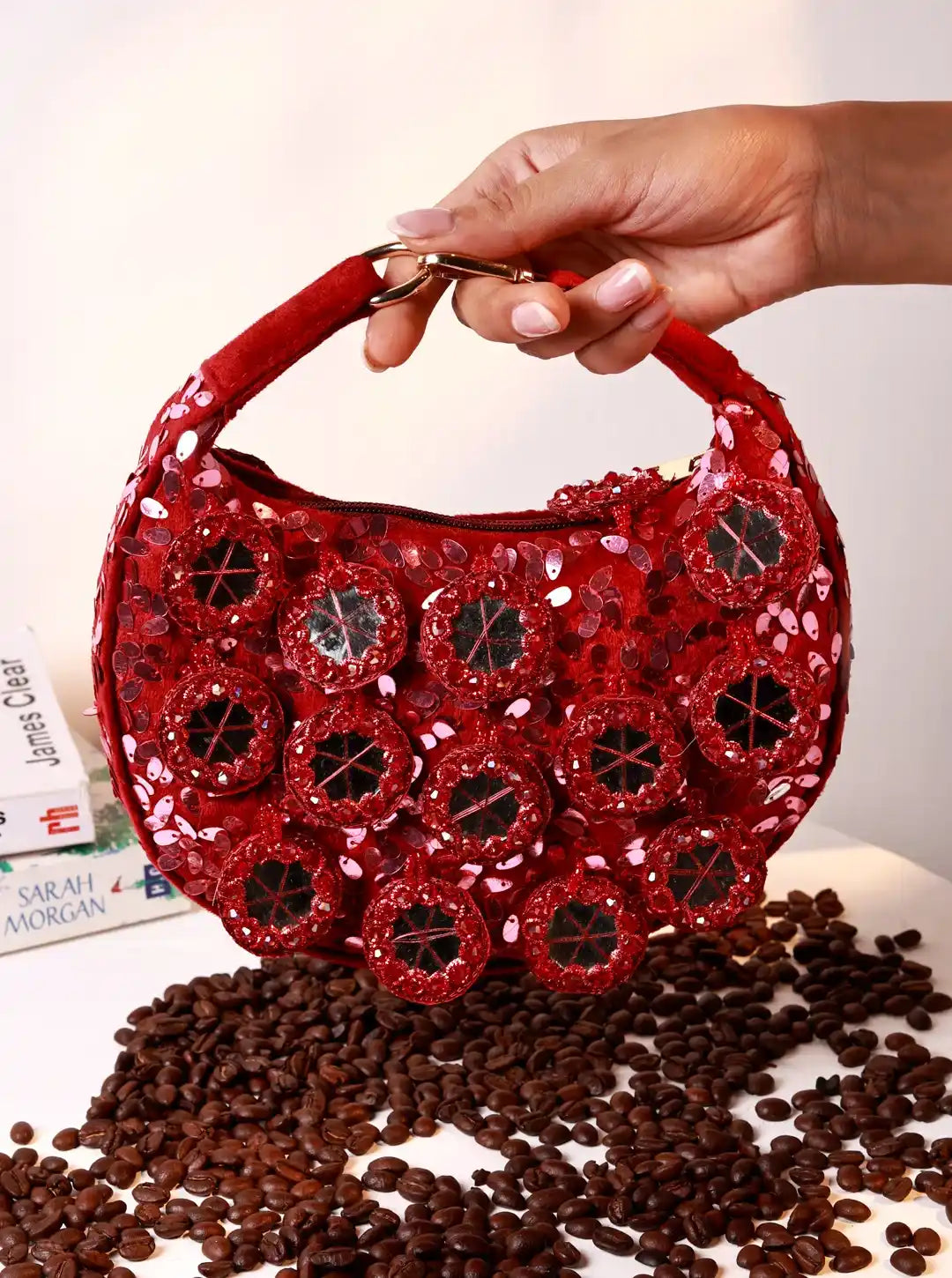 Red sequined handbag held by a hand on a white background with coffee beans.