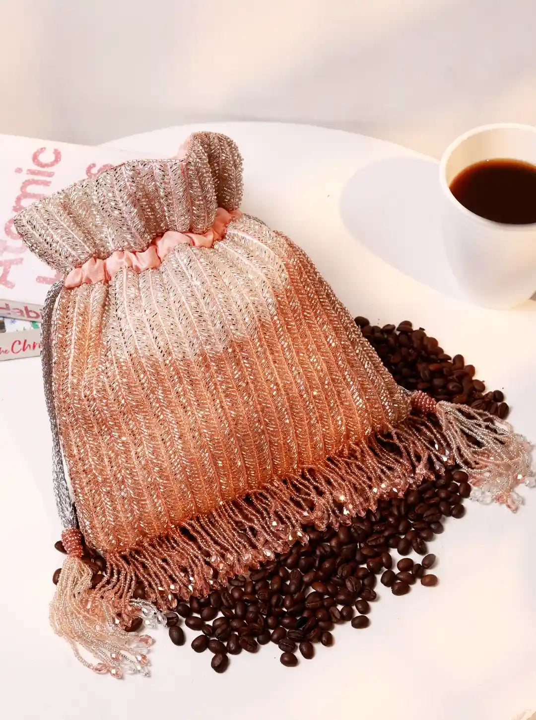 Decorative drawstring bag with coffee beans and a cup of coffee on a light surface.