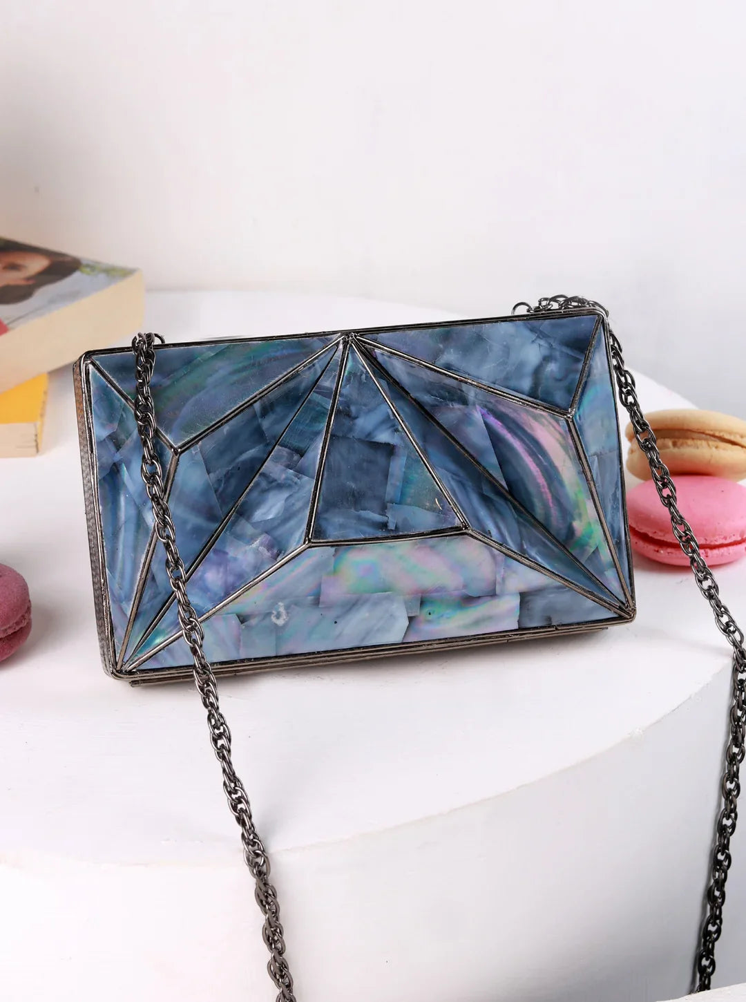 Blue geometric handbag with chain strap on a white surface