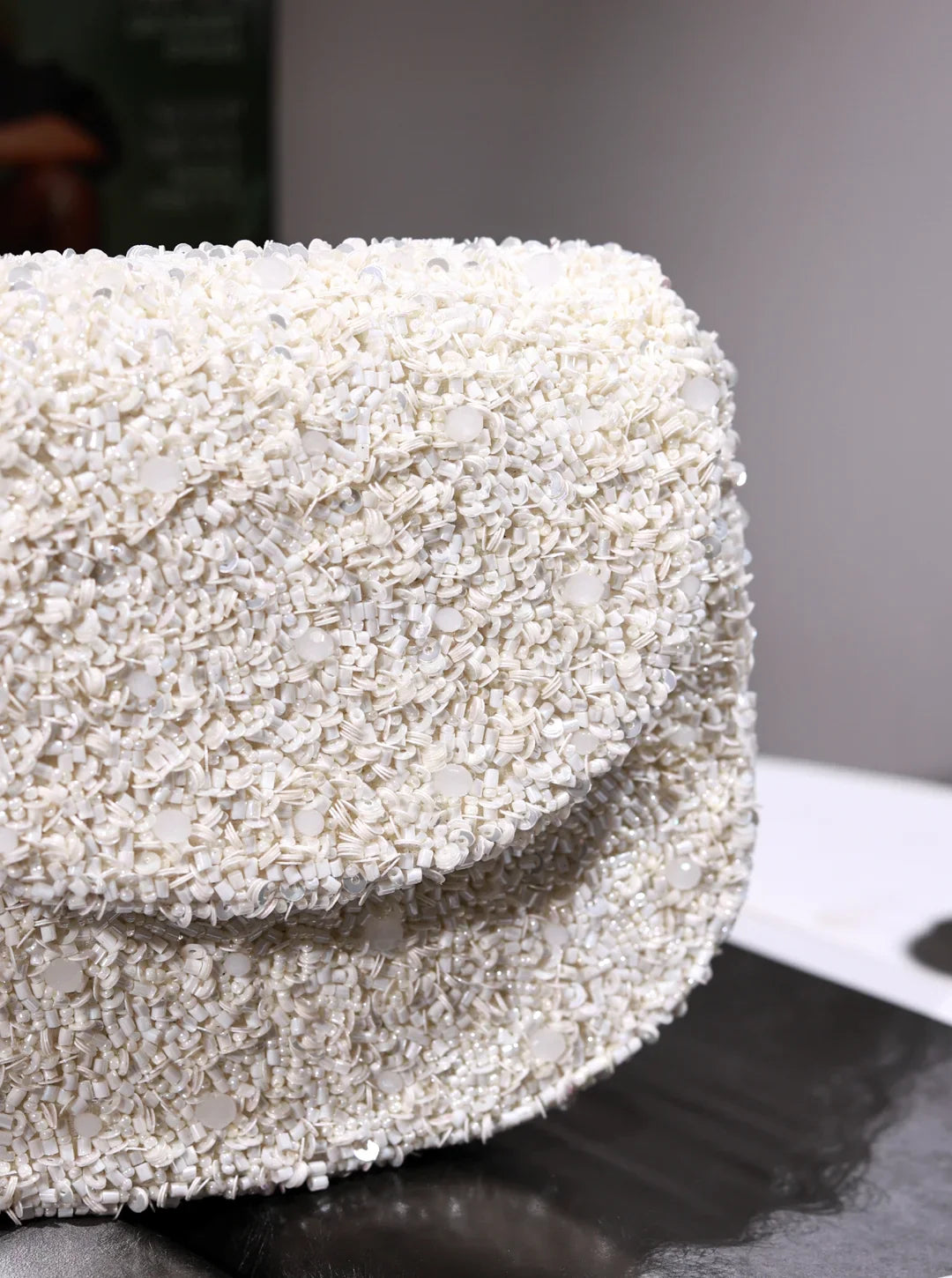 Close-up of a textured white handbag on a dark surface with a blurred background