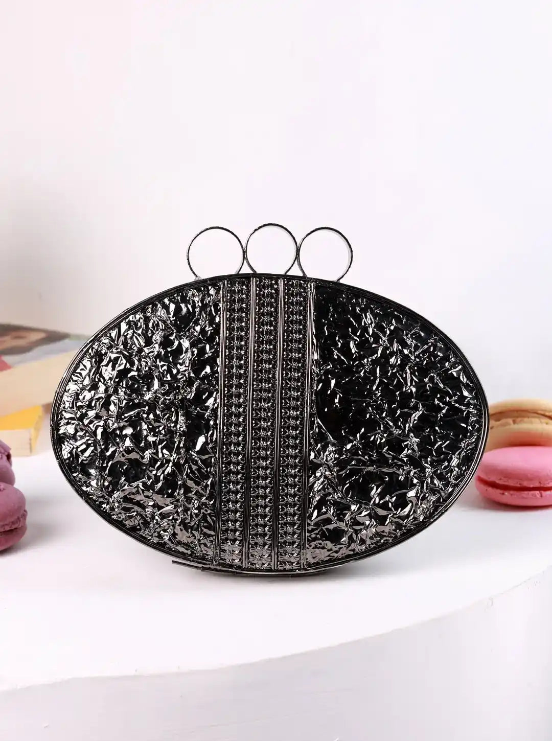 Black textured clutch bag on a white surface with pink macarons in the background